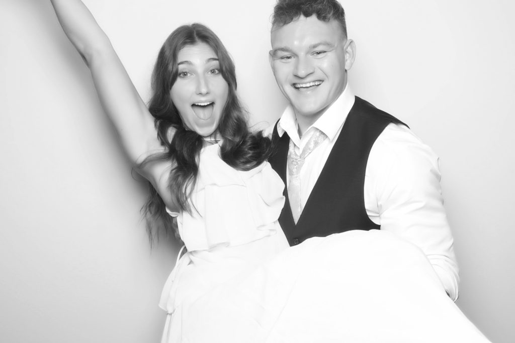 Black and white glam photo booth picture of a man lifting a cheering woman in a white dress