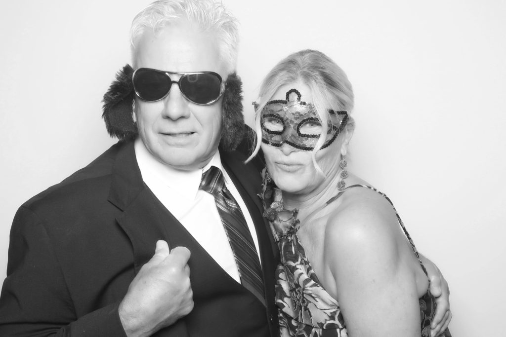 Black and white glam photo booth picture of a couple in oversized sunglasses and a masquerade mask